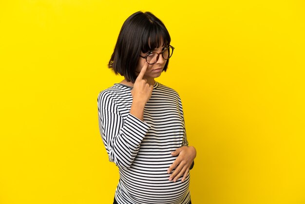 Young pregnant woman over isolated yellow background showing something