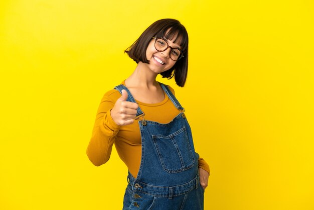 Young pregnant woman over isolated yellow background with thumbs up because something good has happened