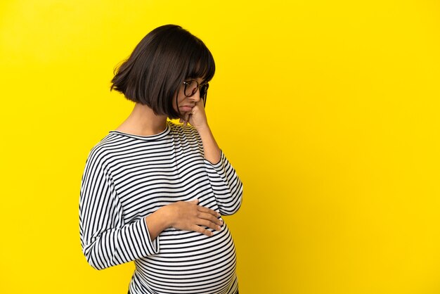 Giovane donna incinta su sfondo giallo isolato con espressione stanca e annoiata