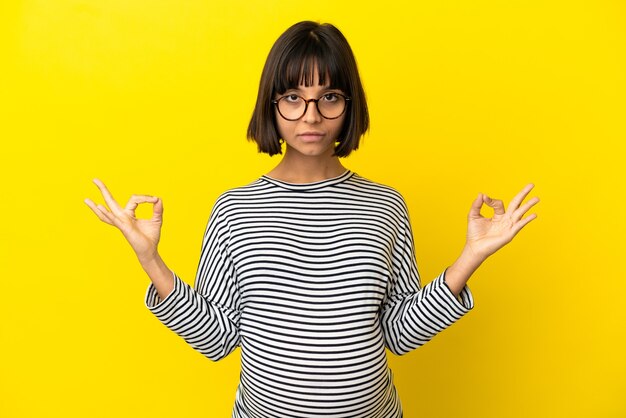 Young pregnant woman over isolated yellow background in zen pose