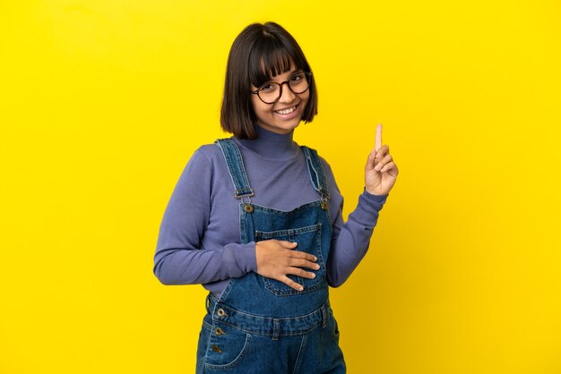 Young pregnant woman over isolated yellow surface pointing up a great idea