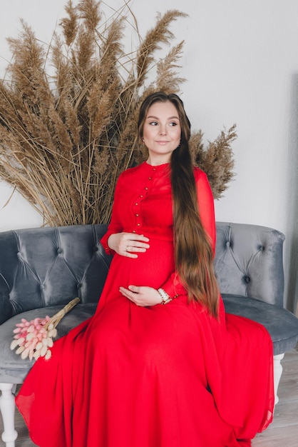 Young pregnant woman in long red dress sitting in studio belly care