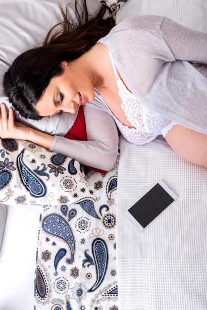 A young pregnant woman lying on a bed with a smartphone next to her