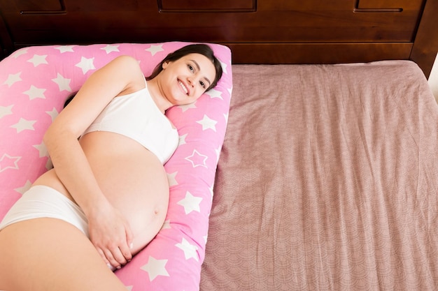 Young pregnant woman lying in bed with supportive pillow