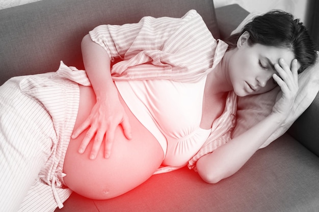 사진 고통스러운 두통으로 집에서 소파에 누워있는 젊은 임산부