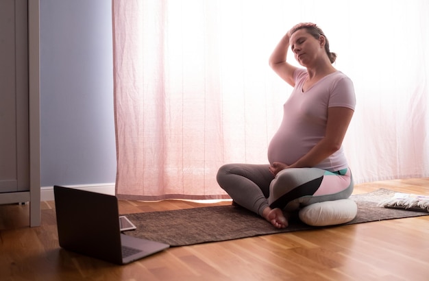 Young pregnant woman practices yoga at home