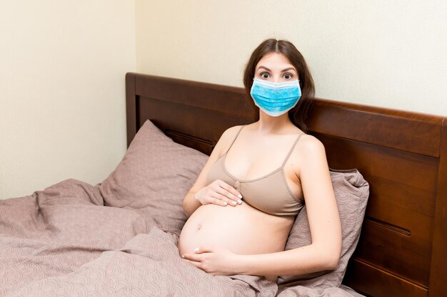 Photo young pregnant woman in protective medical mask is staying in bed because of coronavirus quarantine