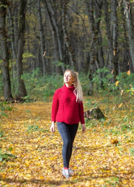 A young pregnant woman in a red sweater among fallen leaves in an autumn forest in a great mood