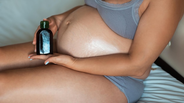 Young pregnant woman rubs massage oil into her belly