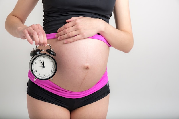 Young pregnant woman in sportswear with alarm clock