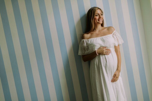 Young pregnant woman standing by the wall