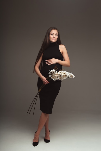 Young pregnant woman stands with a flower in a black dress