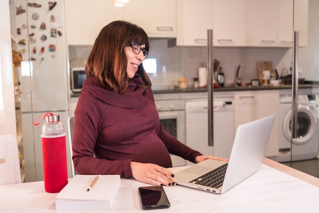 Young pregnant woman teleworking with the computer from home due to the difficulties of working, making a video call