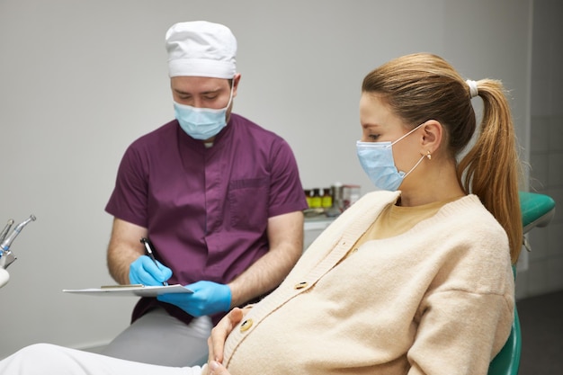 Young pregnant woman wearing medical mask at dentist appointment in dentistry clinic