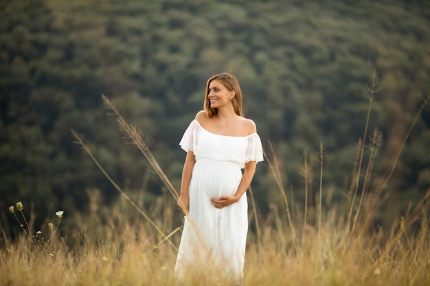 Giovane donna incinta in abito bianco presso il campo estivo