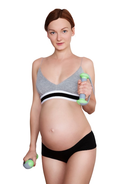 Молодая беременная женщина с красивым здоровым телом, держащая гантели и циновку