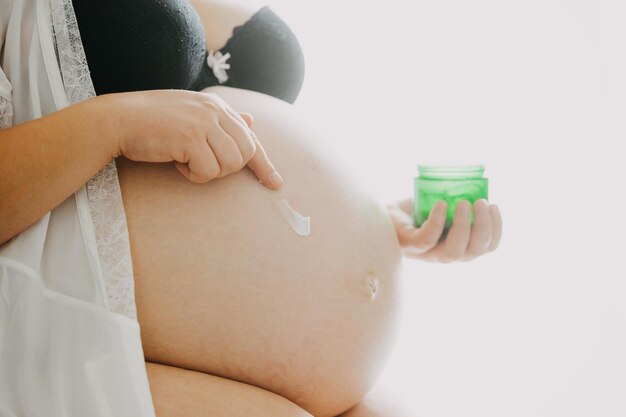 妊娠線の妊娠概念に対してクリームを腹に塗る若い妊婦