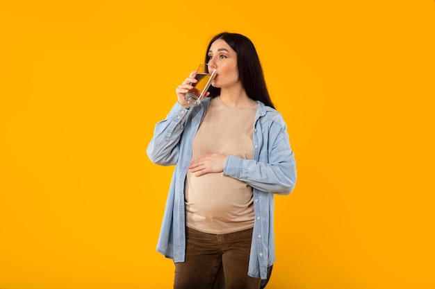 Young pregnant woman with big belly drinking glass of water enjoying future motherhood standing on