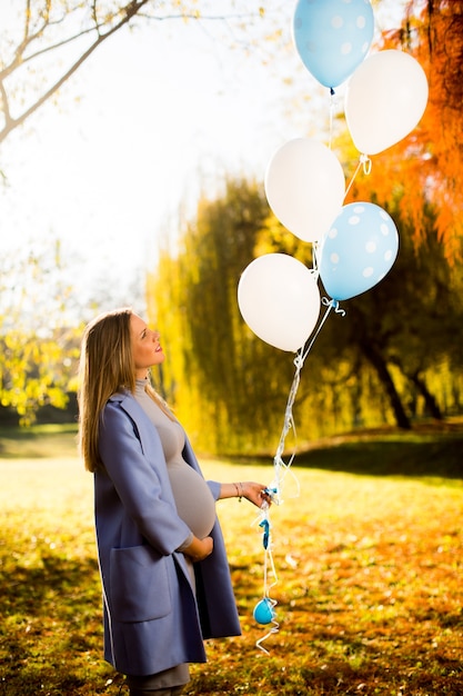 Young pregnant woman with colorful balloons in autumn forest