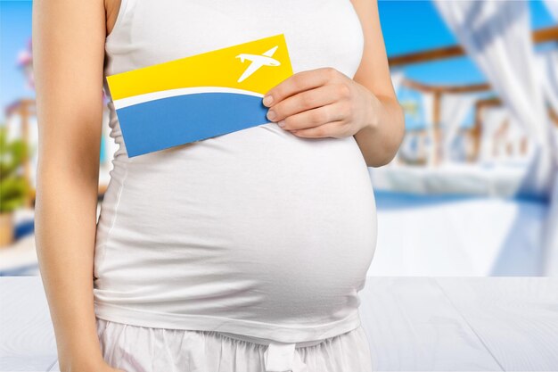 Young pregnant woman with flight ticket on blurred background