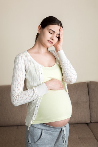 Young pregnant woman with headache sitting on sofa Pregnancy expectation concept