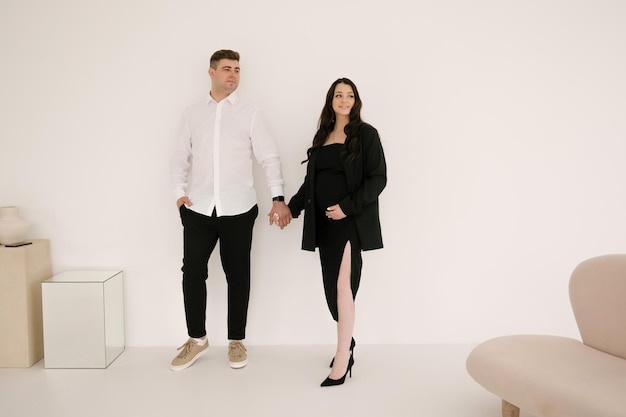 Young pregnant woman with her husband in stylish elegant black clothes on a light background