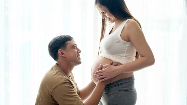 Молодая беременная женщина с мужем обнимаются и ждут ребенка дома