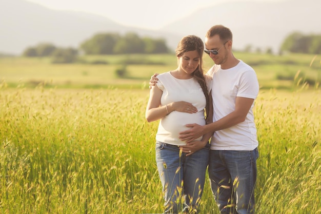 Young pregnant woman with husband enjoying the nature wearing casual clothes Family look