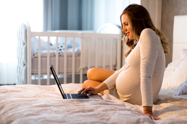 Giovane donna incinta con il computer portatile nel letto