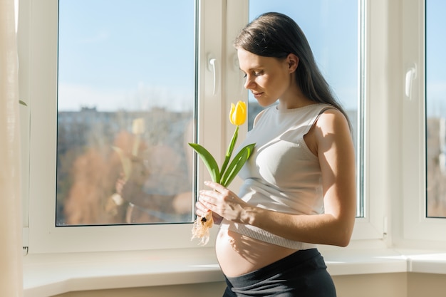 黄色のチューリップの花を持つ若い妊娠中の女性