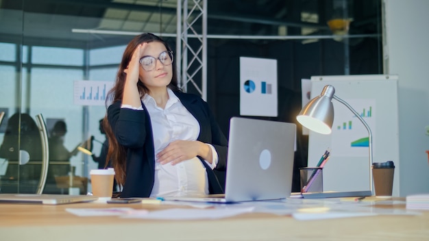 Giovane donna incinta che lavora nell'ufficio moderno sente dolore stanca donna d'affari incinta incinta...