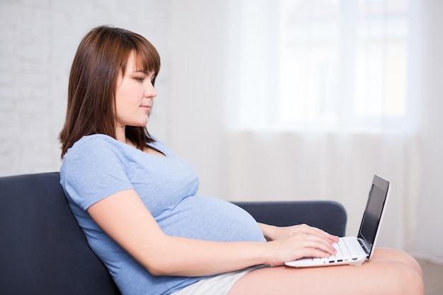 Молодая беременная женщина, работающая с ноутбуком в яркой гостиной