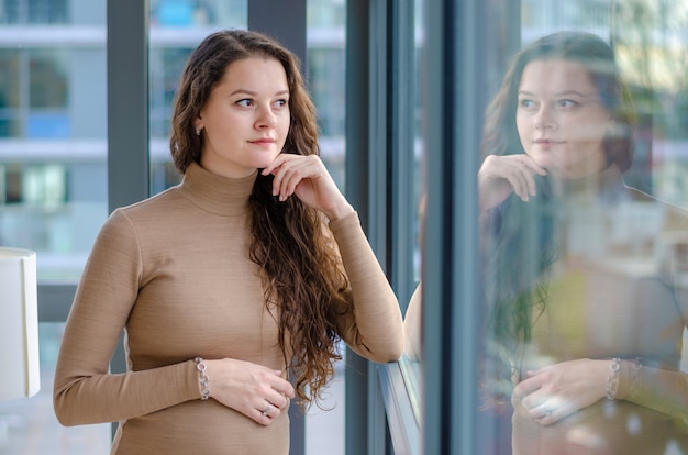 Young pregnant young woman enjoying sunny morning near big window in home