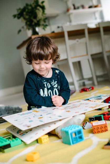 Young preschool boy reading book on the floor at home