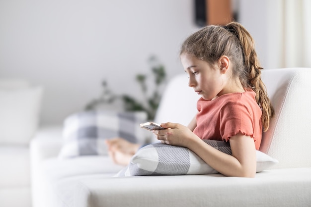 Молодая девочка-подросток смотрит в свой телефон, комфортно проводя время дома