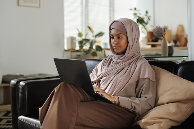 Молодая красивая афроамериканка в хиджабе печатает на клавиатуре ноутбука