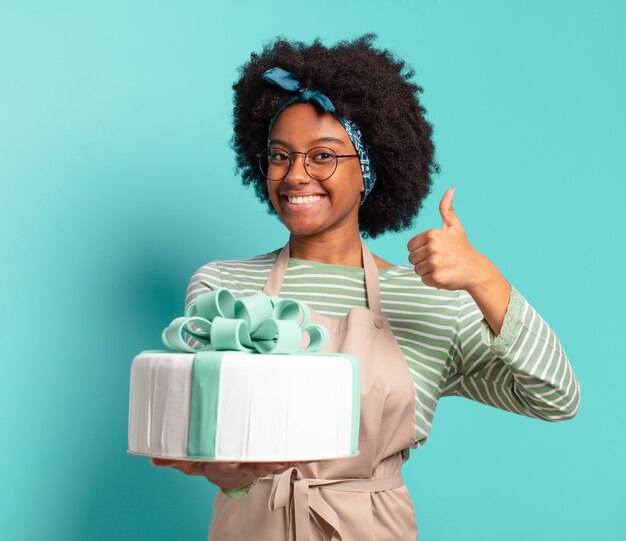 Giovane bella panettiera afro con una torta di compleanno