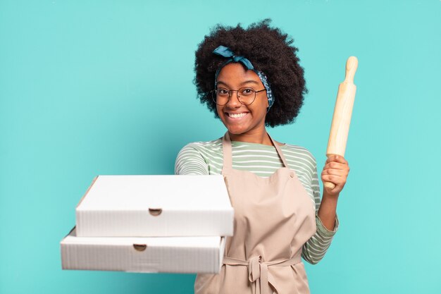 Young pretty afro woman chef with a rolling pin and pizzas