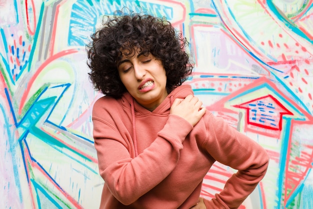 Photo young pretty afro woman feeling tired, stressed, anxious, frustrated and depressed, suffering with back or neck pain against graffiti wall