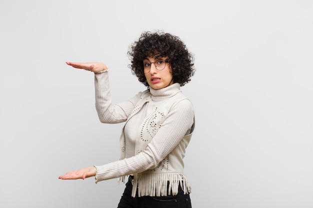 Young pretty afro woman holding an object with both hands on side copy space, showing, offering or advertising an object