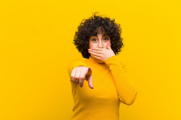 Young pretty afro woman laughing at you, pointing to and making fun of or mocking you