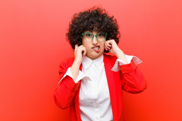 Photo young pretty afro woman looking angry, stressed and annoyed, covering both ears to a deafening noise, sound or loud music