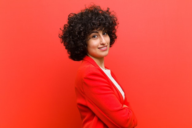 Young pretty afro woman smiling to camera with crossed arms and a happy, confident, satisfied expression, lateral view