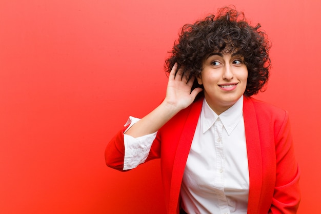 Young pretty afro woman smiling, looking curiously to the side, trying to listen to gossip or overhearing a secret