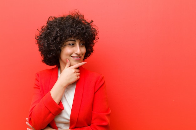 Young pretty afro woman smiling with a happy, confident expression with hand on chin, wondering and looking to the side