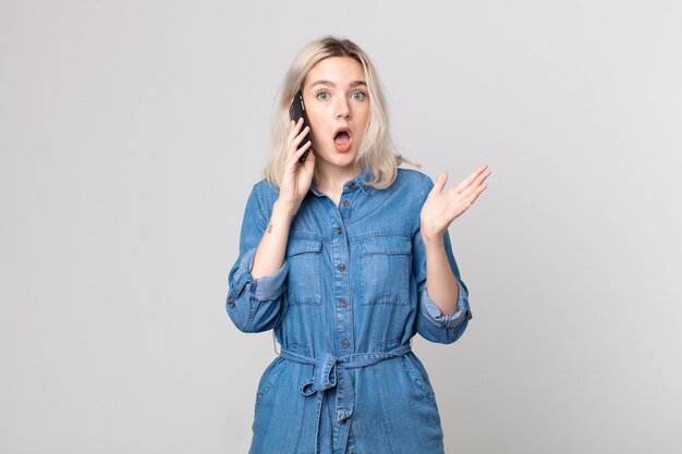 Young pretty albino woman amazed, shocked and astonished with an unbelievable surprise and talking with a smartphone