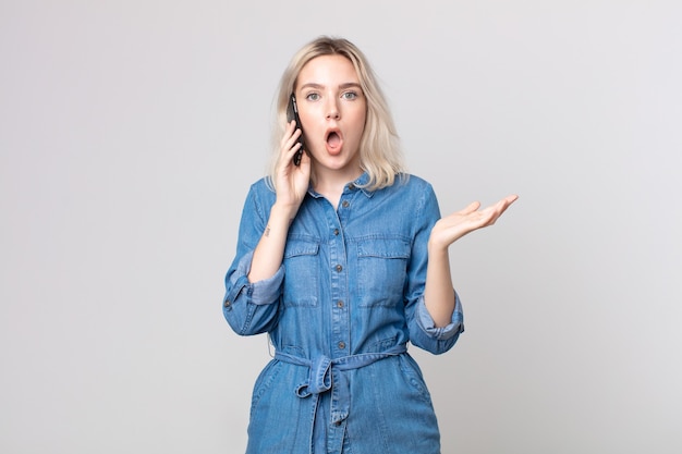 Young pretty albino woman feeling extremely shocked and surprised and talking with a smartphone