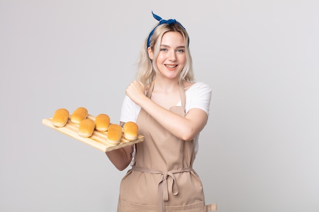 Young pretty albino woman feeling happy and facing a challenge or celebrating with a bread buns tray