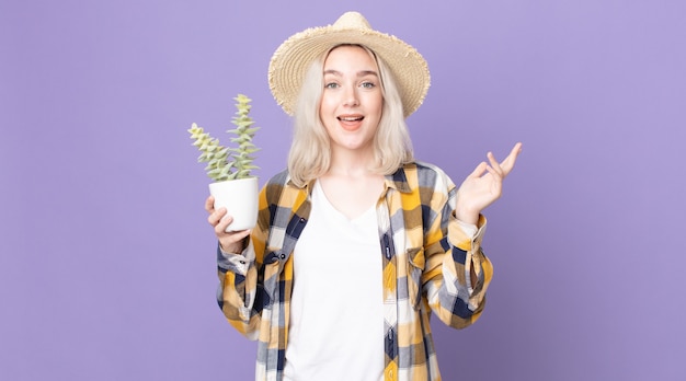 Молодая красивая женщина-альбинос чувствует себя счастливой, удивленной, осознавая решение или идею и держа кактус комнатное растение