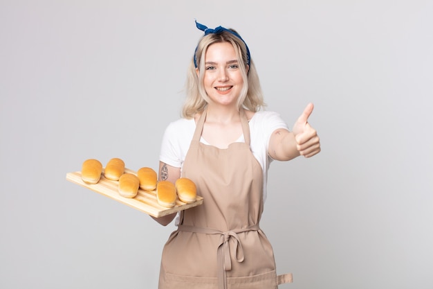 Young pretty albino woman feeling proud,smiling positively with thumbs up with a bread buns tray
